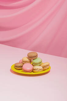 Delicious sweet multicolored macaroons placed on bright yellow round shaped plate against pink background - ADSF44644