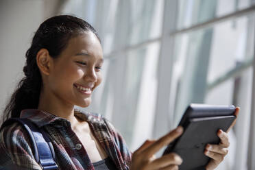 Lächelnder Student, der einen Tablet-PC in der Universität benutzt - IKF00969