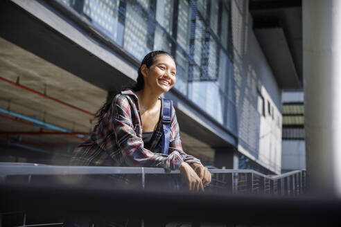 Smiling student standing near university railing - IKF00977