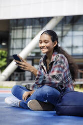 Lächelnder Student mit Smartphone vor der Universität - IKF00982