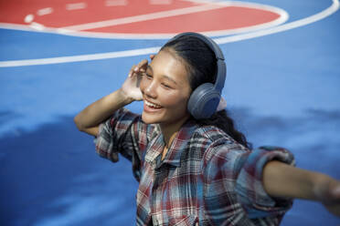 Smiling student listening to music in playground - IKF00983