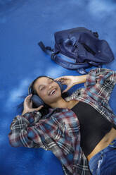 Smiling student lying down and listening to music - IKF00985