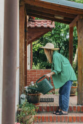 Frau bewässert Pflanzen vor dem Haus - VSNF01120