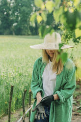 Woman with hat wearing gloves in garden - VSNF01126