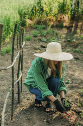 Woman with sun hat planting in garden - VSNF01127