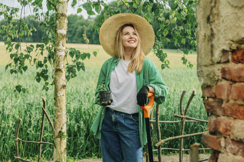 Lächelnde Frau hält Topfpflanze im Garten - VSNF01129