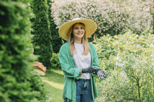 Smiling woman wearing gloves in garden - VSNF01130