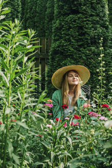 Lächelnde Frau riecht an Blumen im Garten - VSNF01131