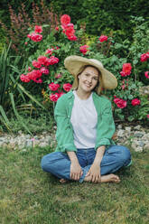 Smiling woman sitting cross-legged on grass in garden - VSNF01136