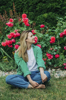 Lächelnde Frau vor Rosenpflanzen im Garten sitzend - VSNF01137
