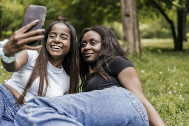 Smiling friends taking selfie through smart phone at park - PBTF00030