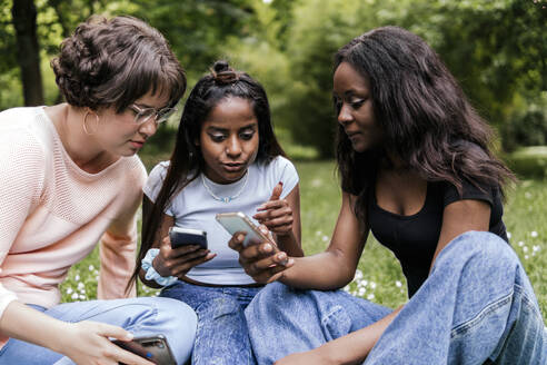 Frau diskutiert mit Freunden über ihr Smartphone im Park - PBTF00033