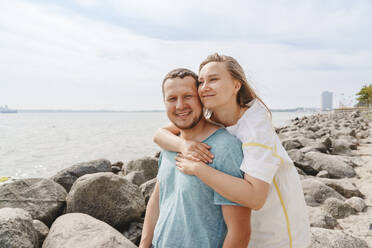 Lächelnde Frau umarmt Mann am Strand - IHF01472