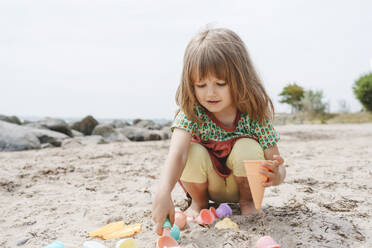 Girl playing in sand with cones at beach - IHF01478