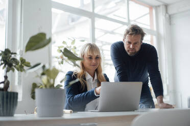 Smiling businesswoman discussing with colleague over laptop - JOSEF19873