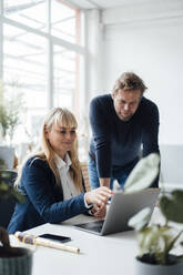 Smiling businesswoman discussing over laptop with businessman in office - JOSEF19874