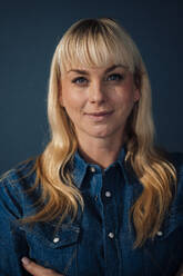 Smiling blond businesswoman against blue background - JOSEF19898