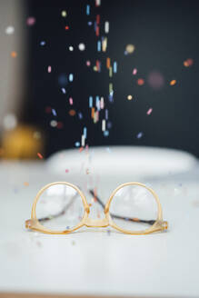 Yellow eyeglasses with multi colored pearls falling on desk - JOSEF19902