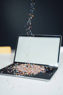 Multi colored pearls falling on laptop at desk - JOSEF19904