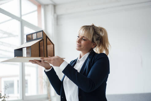 Blonde Geschäftsfrau, die ein Modellhaus im Büro untersucht - JOSEF19918