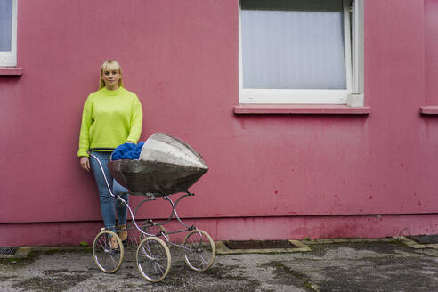 Woman with baby stroller standing in front of pink wall - JOSEF19923