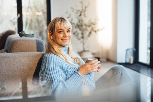 Glückliche Frau mit Kaffeetasse im Wohnzimmer sitzend zu Hause - JOSEF19927