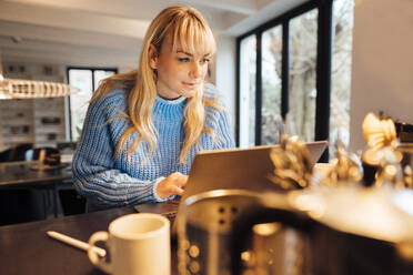 Freelancer with blond hair working on laptop at home - JOSEF19936