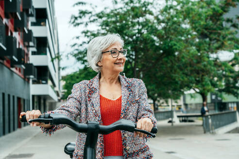 Senior businesswoman wheeling bicycle on street - GDBF00073