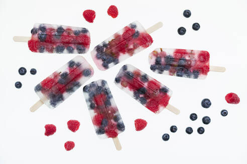 Studio shot of homemade popsicles with fresh raspberries, blueberries and gooseberries lying against white background - GWF07851