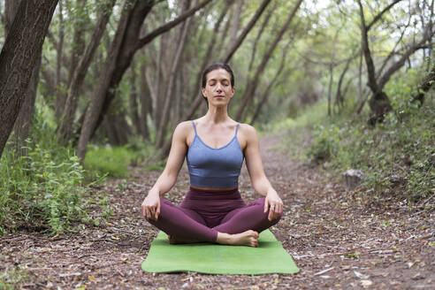 Frau meditiert auf Übungsmatte im Wald - LMCF00293