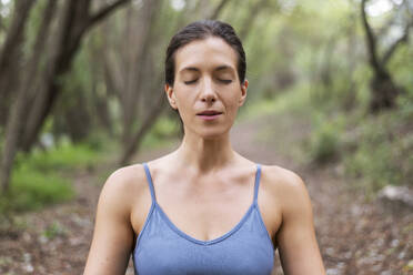 Frau meditiert mit geschlossenen Augen im Wald - LMCF00294
