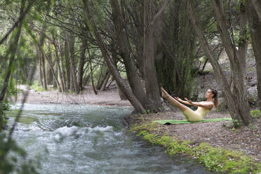 Woman doing Pilates near stream at forest - LMCF00297