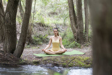 Frau meditiert in der Nähe eines Baches im Wald - LMCF00298