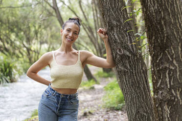 Smiling woman leaning on tree in forest - LMCF00303