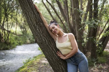 Lächelnde Frau lehnt an einem Baum im Wald - LMCF00306