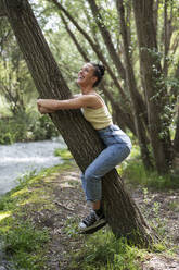 Happy woman embracing tree in forest - LMCF00307