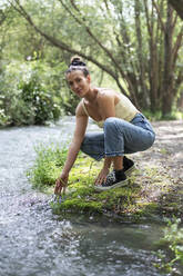 Smiling woman spending leisure time near stream in forest - LMCF00309
