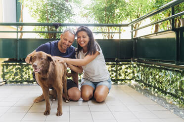 Smiling couple spending leisure time with dog in balcony - MEUF09156