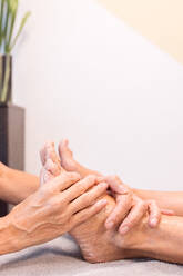 Anonymous therapist holding foot of unrecognizable client with hands and massaging with fingers to relieve pain by gently pressing pressure points in sole in parlor - ADSF44656