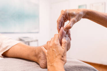 Anonymous therapist holding foot of unrecognizable client with hands and massaging with fingers to relieve pain by gently pressing pressure points in sole in parlor - ADSF44657