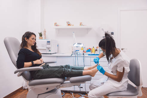 Professional female podiatrist in medical mask and latex gloves doing pedicure with special equipment in modern clinic - ADSF44674