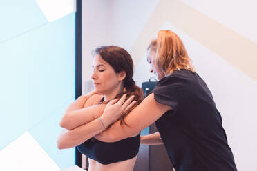 Confident female therapist in black uniform massaging back of patient during rehabilitation session on medical table in modern salon - ADSF44679