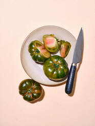 Green tomatoes in bright sunlight flat lay over plate with knife with copy space on beige background - ADSF44683