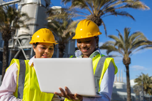 Builders in hardhat and engineer vest standing near construction site with laptop while discussing project - ADSF44701