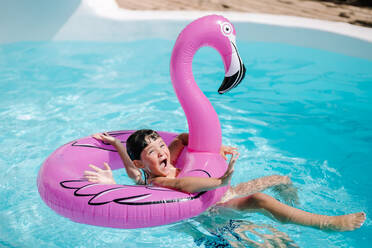 Girl swimming with flamingo pink inflatable ring in clean pool water while having fun during vacation - ADSF44805
