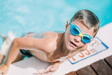 From above of little boy in swimming glasses and swimwear getting out on poolside while enjoying summer holidays during vacation - ADSF44806