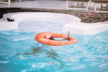 Unrecognizable girl with orange inflatable tube swimming underwater in clear pool water during summer holidays - ADSF44808