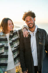 Positive multiracial couple in casual clothes standing together and smiling while enjoying time on sunny day during date - ADSF44836