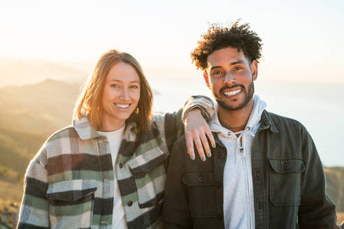 Positive multiracial couple in casual clothes standing together and smiling while enjoying time on sunny day during date - ADSF44837