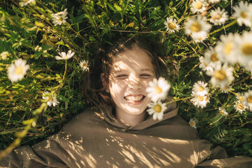 Smiling boy lying amidst daisies in field - ANAF01725